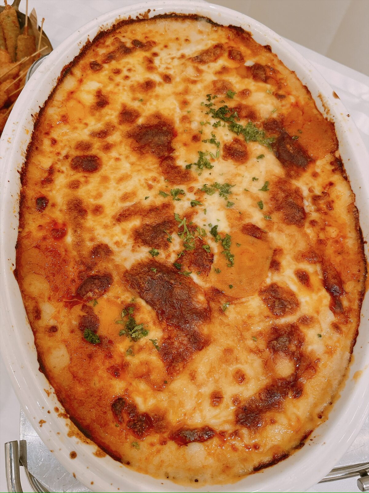 白い耐熱皿で焼かれた、チーズがこんがりしたラザニア