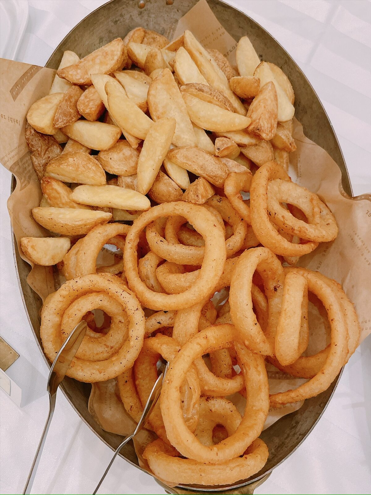 木の大皿に、くし形のフライドポテトとオニオンリングが盛られている