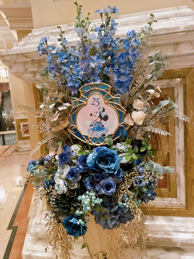 青い花のアレンジメントに添えられた25周年のミニーのプレート