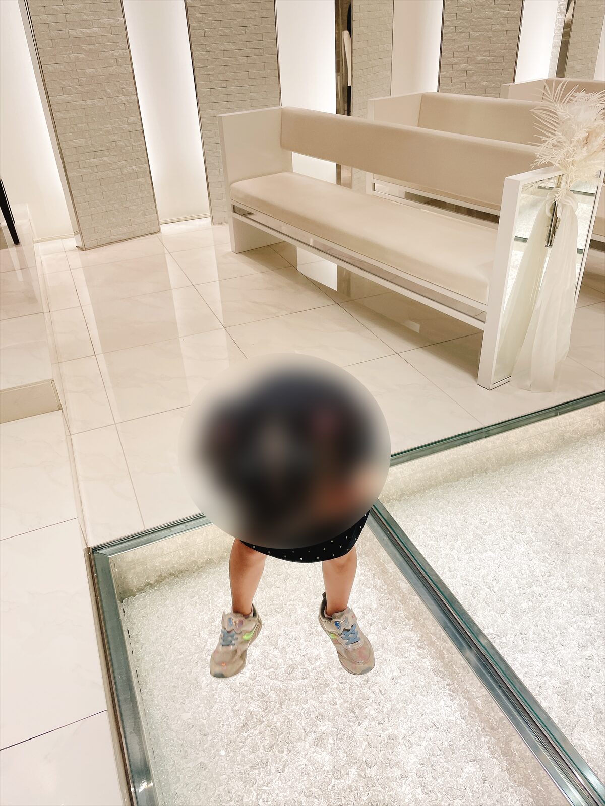 ガラスの床の上に立つ子どもを真上から見た写真。ガラスの下に細かい石が敷き詰められている（顔はぼかし処理）