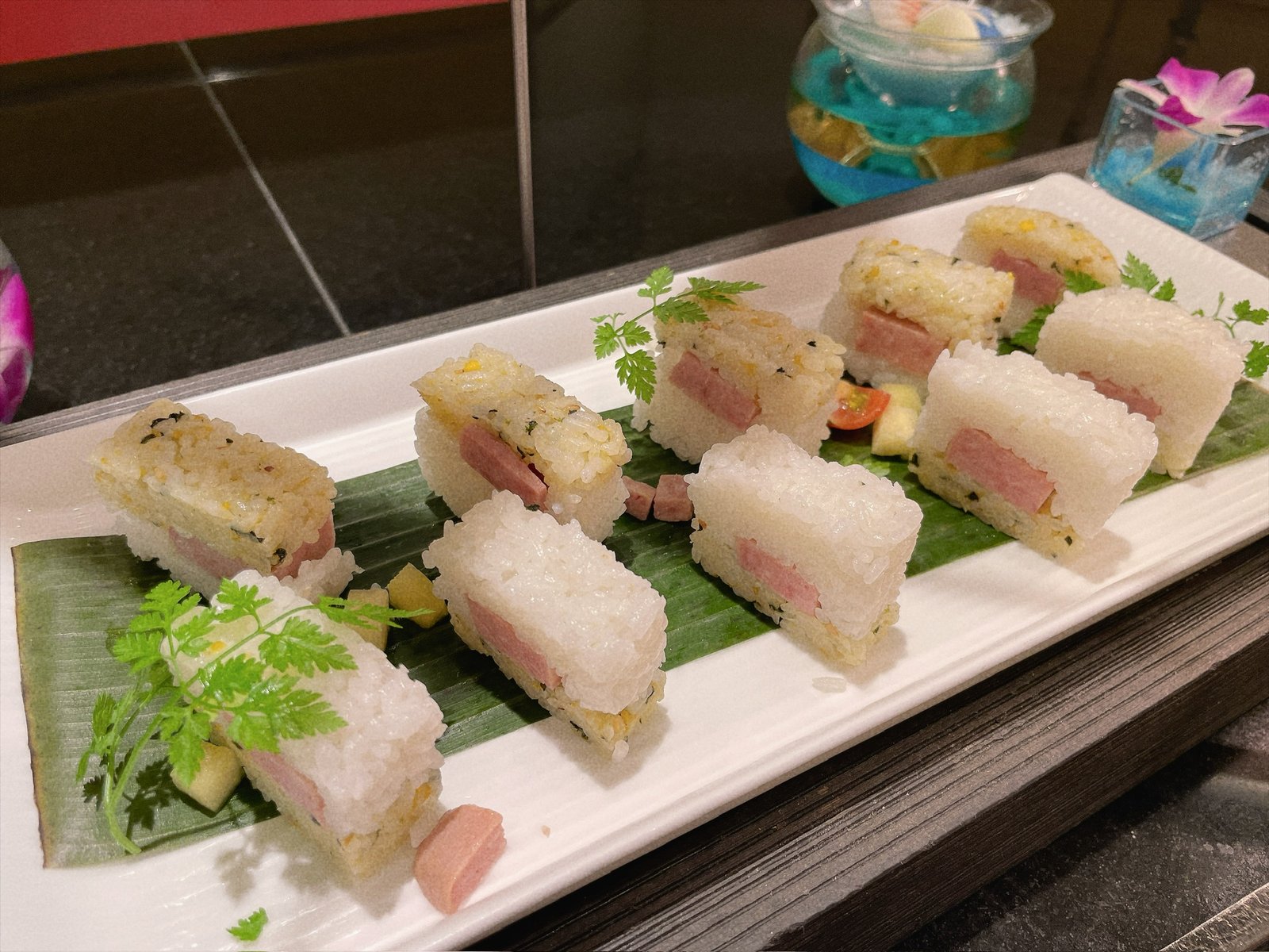 長い白い皿に並んだスパムライス。俵形のごはんの間に、焼いたスパムが挟まれている