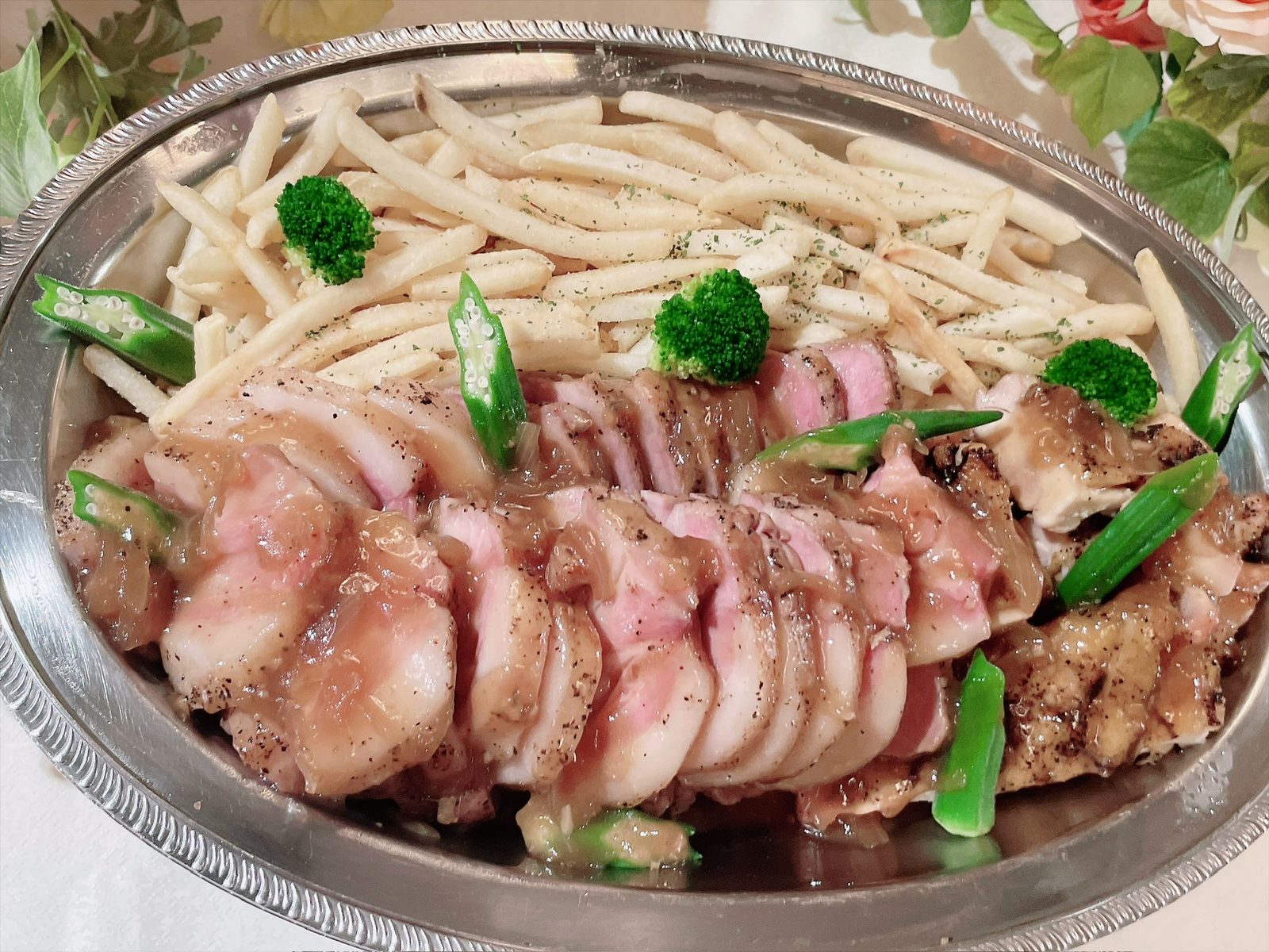 銀色の楕円皿に切り分けられた肉料理が並び、奥にフライドポテト、間にオクラとブロッコリーが添えられている