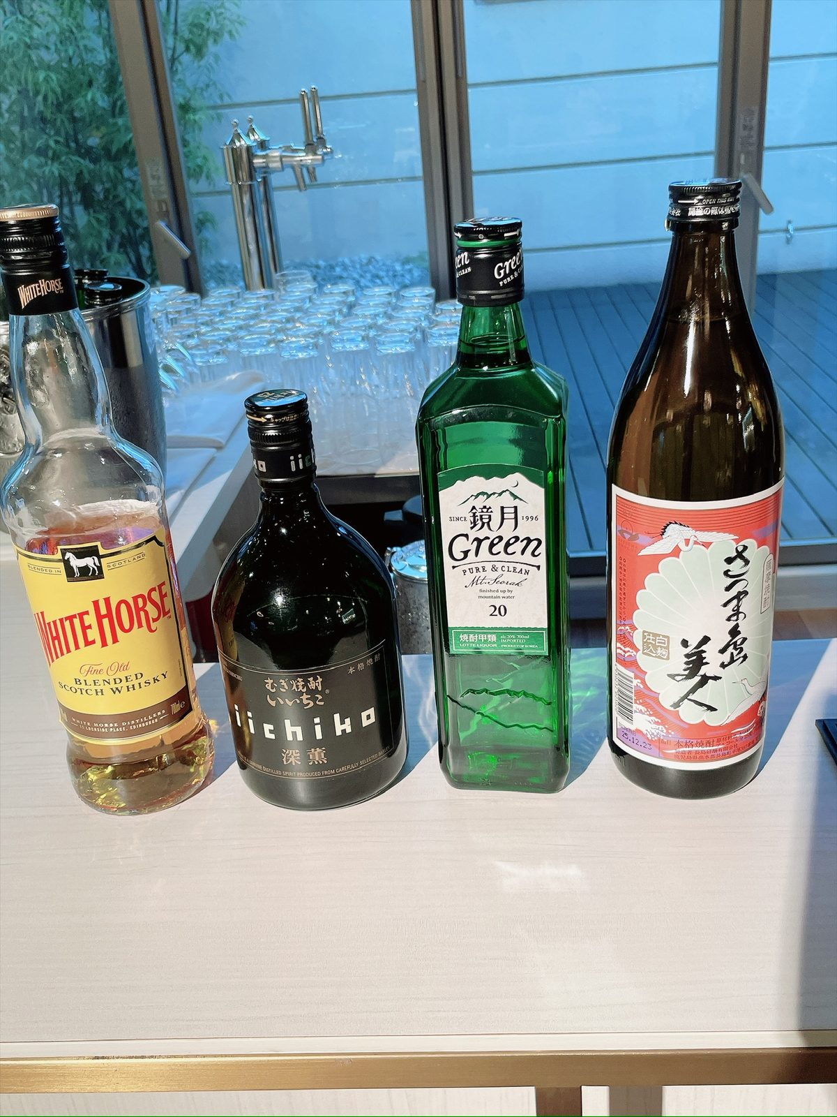 カウンターに並んだ4本の酒瓶。左端にウイスキーのホワイトホース、続いて焼酎のいいちこ、鏡月Green、さつま島美人が並ぶ