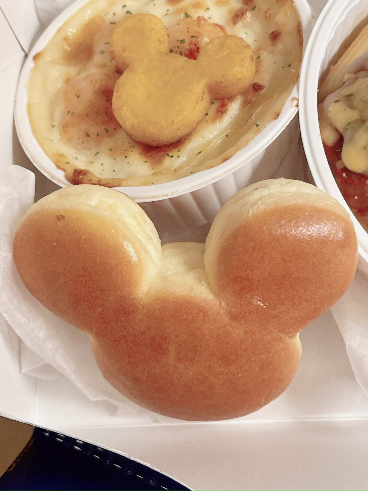 ミッキーの顔の形に焼かれた、つやのあるパンのアップ。奥のグラタンにも、ミッキーの形の薄いチップがのっている