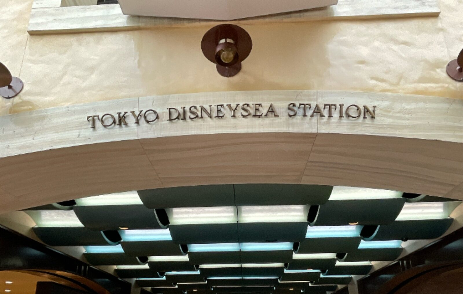 石造りの壁に「TOKYO DISNEYSEA STATION」の文字。その下に格子状の天井と照明が続いている