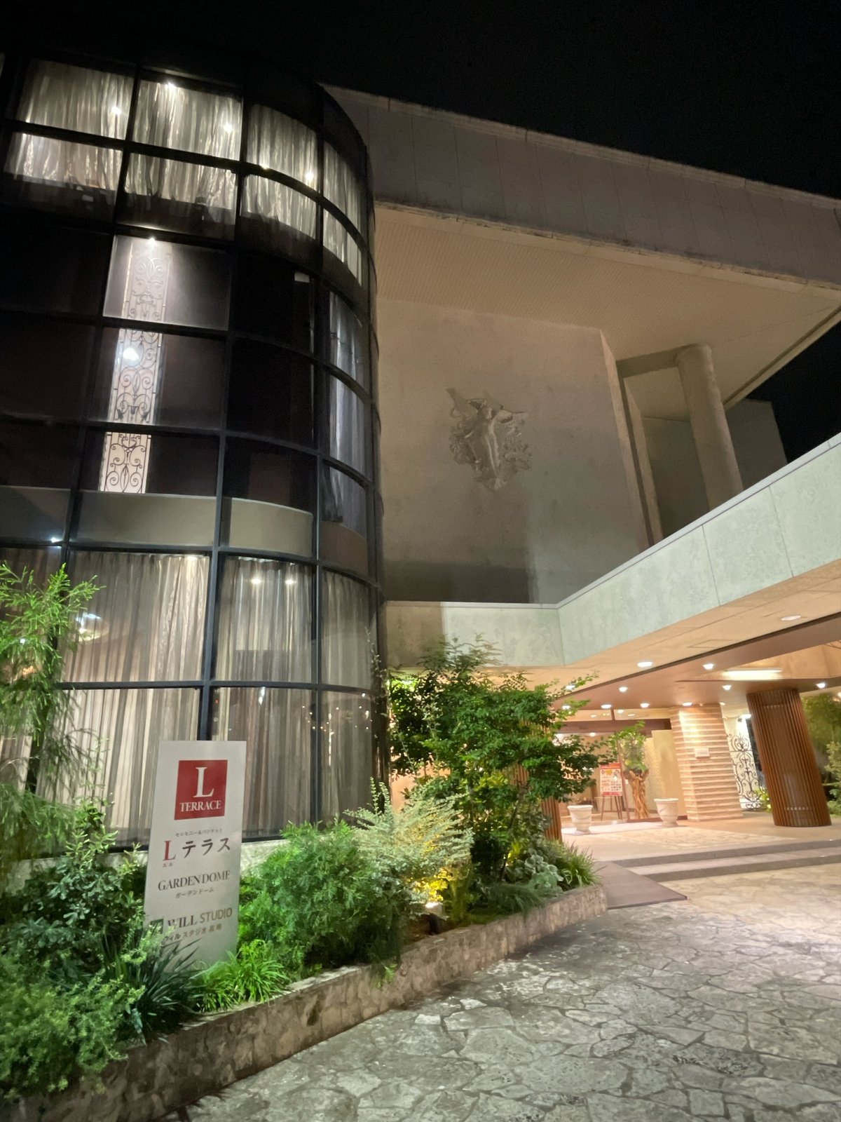 夜のLテラスの外観。曲面のガラス張りの塔と、足元にLテラスの立て看板