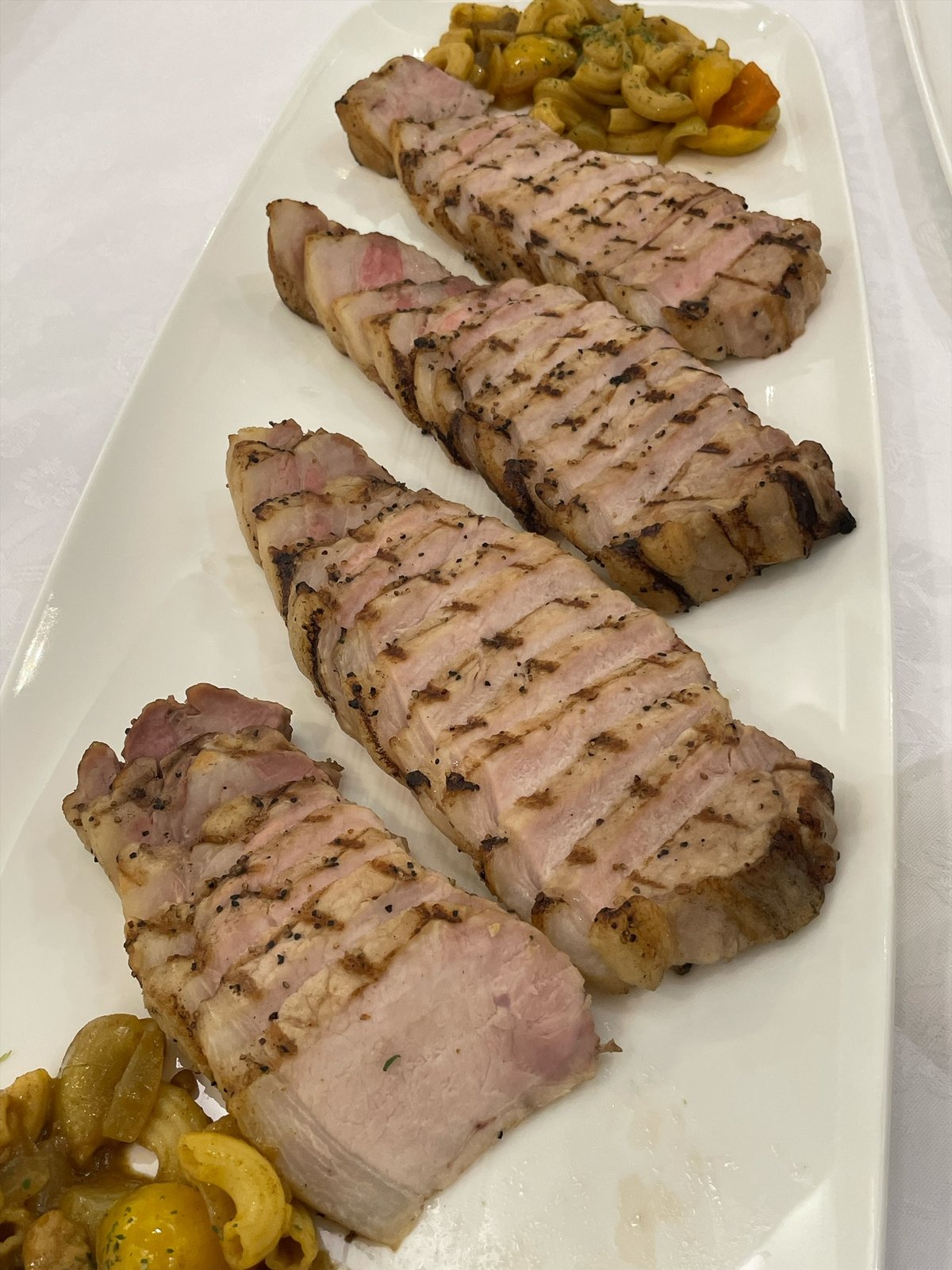 網目の焼き色がついた厚切りの豚肉が、白い大皿に並んでいる。脇にナッツのような添えもの