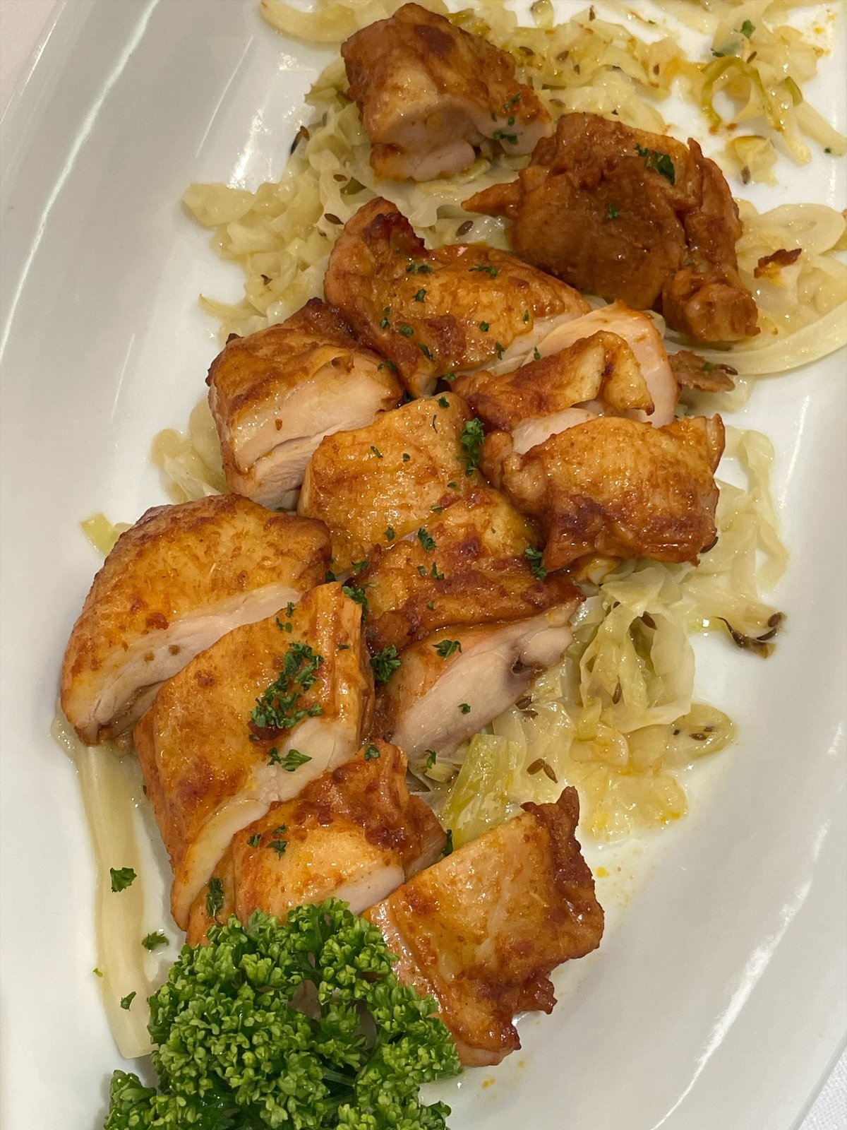 オレンジ色に焼き上がった鶏肉が、千切りの白い野菜の上に盛られている。手前に刻んだパセリ
