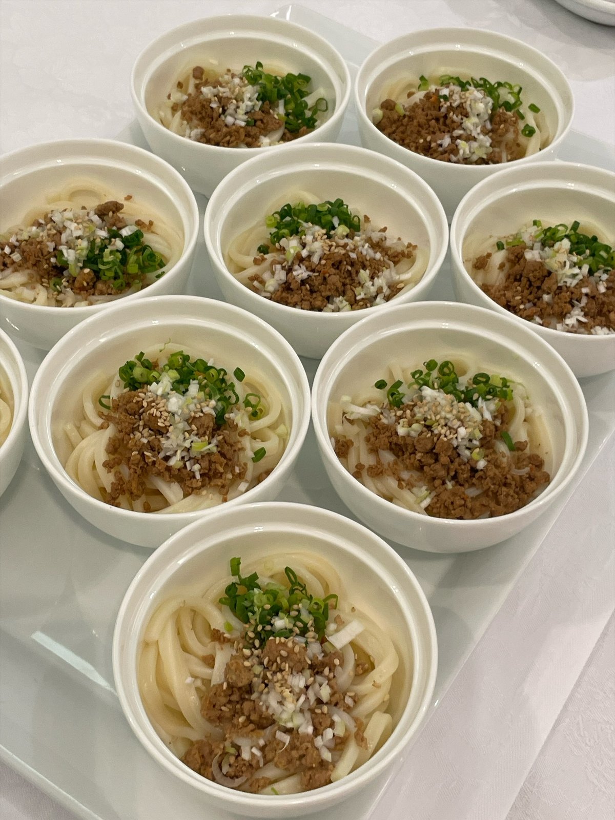 小さな白い器に1人分ずつ盛られたうどん。上にひき肉と刻んだ青ねぎ