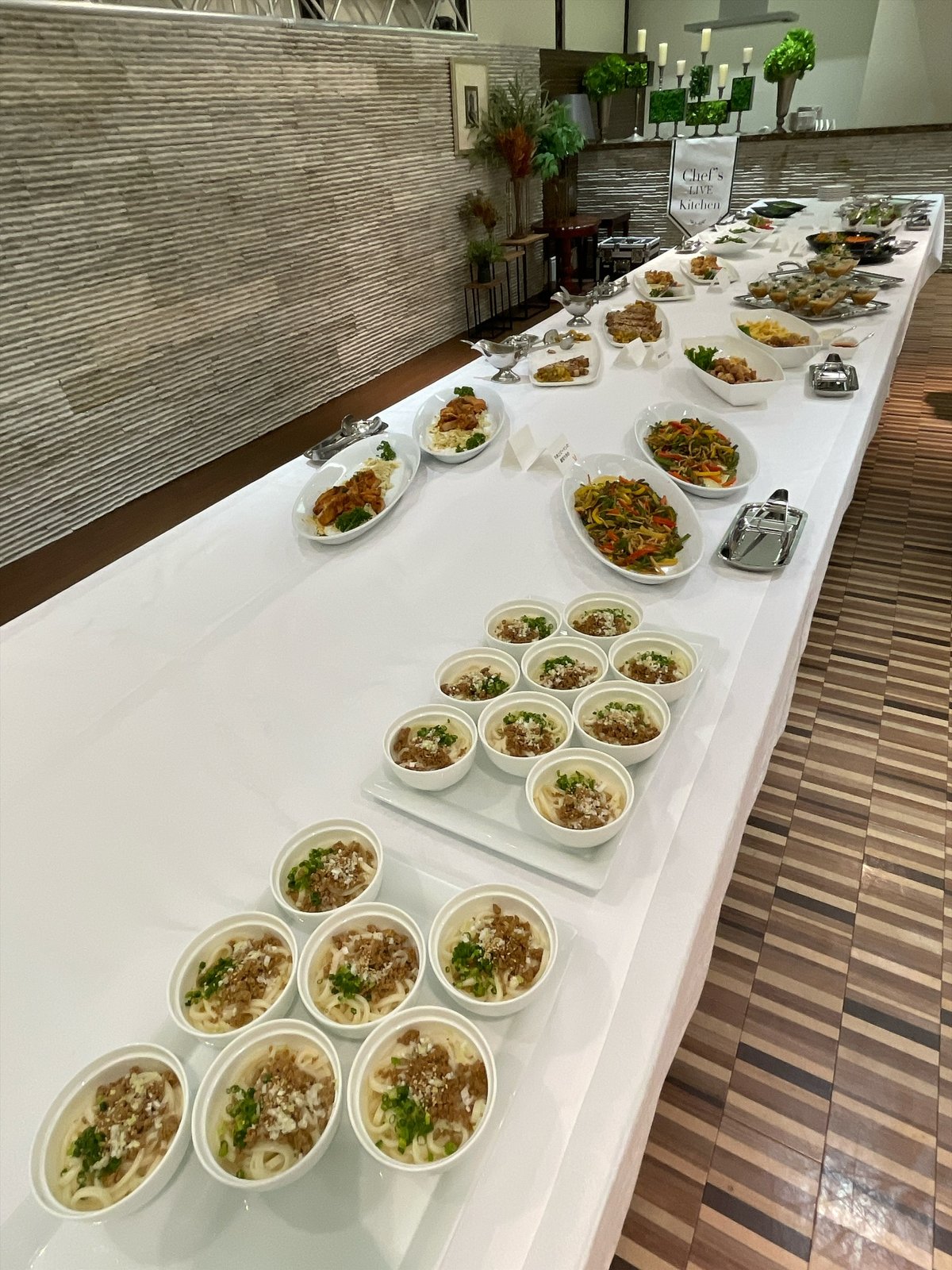 白いクロスの長いビュッフェ台に料理の大皿が並ぶ