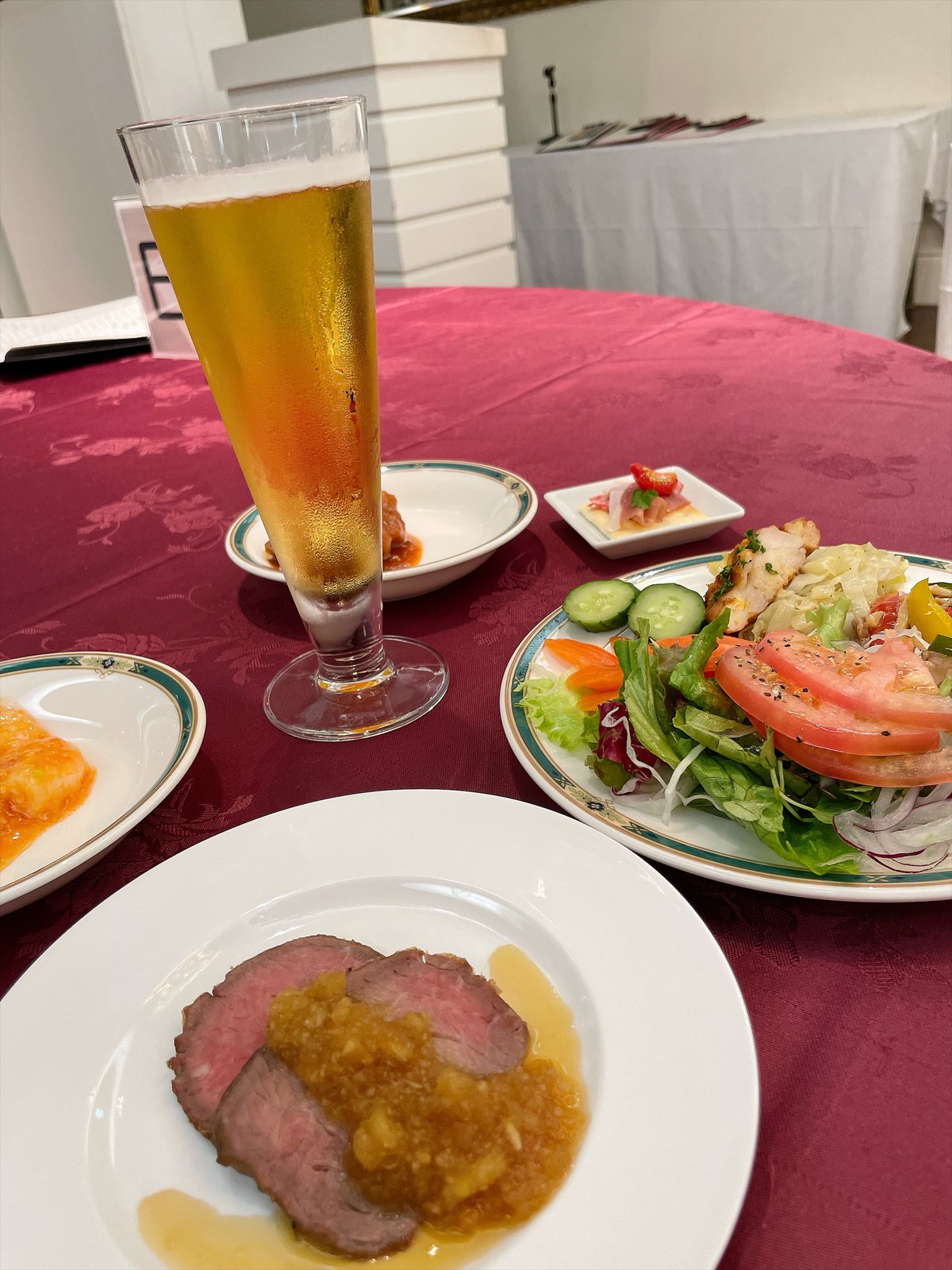 脚つきの細長いグラスに注がれた生ビール。手前にローストビーフの皿、奥にサラダと前菜の皿