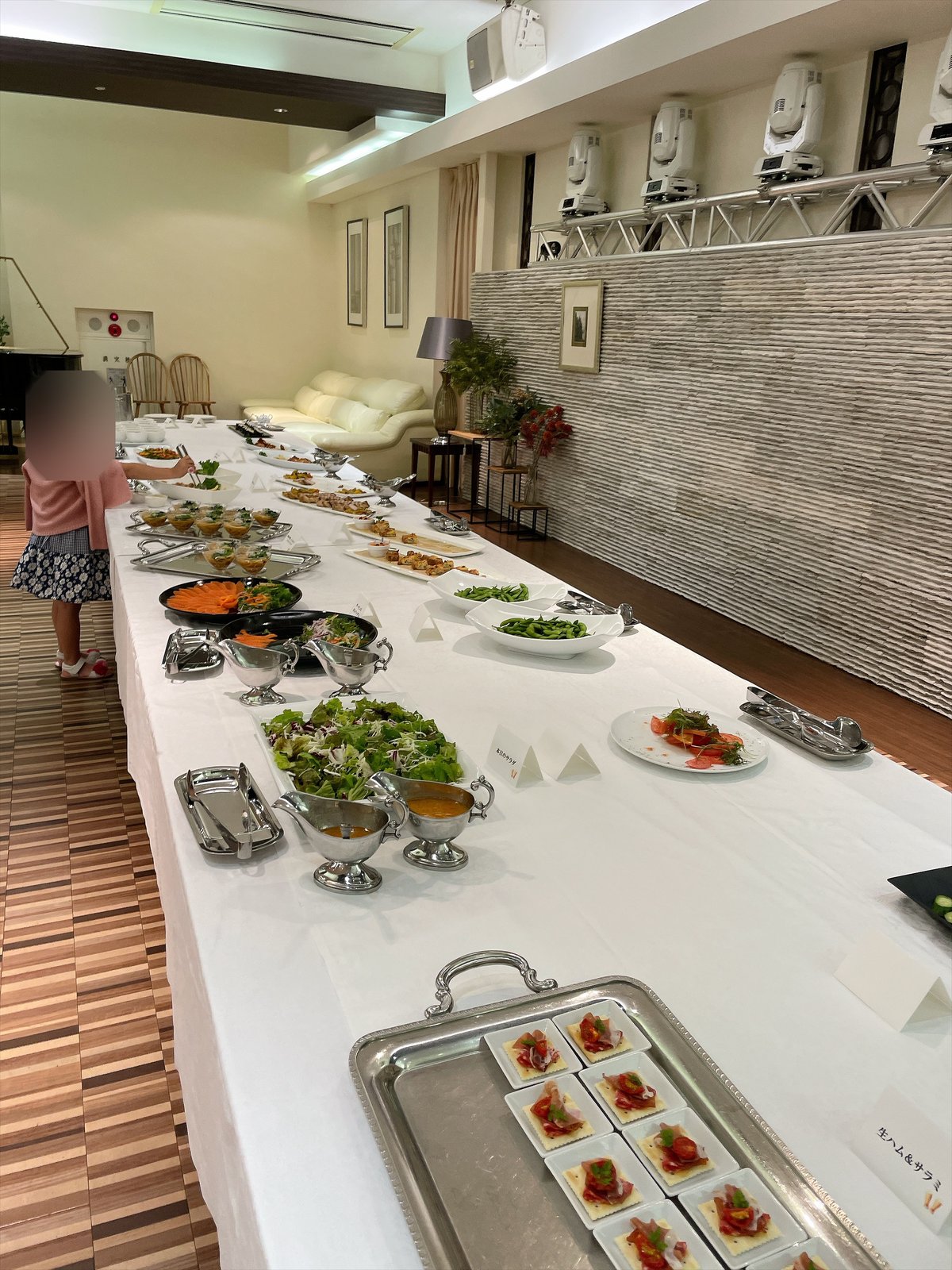 長いビュッフェ台の端に立ち、料理を取っている子ども。顔と髪はぼかしてあります