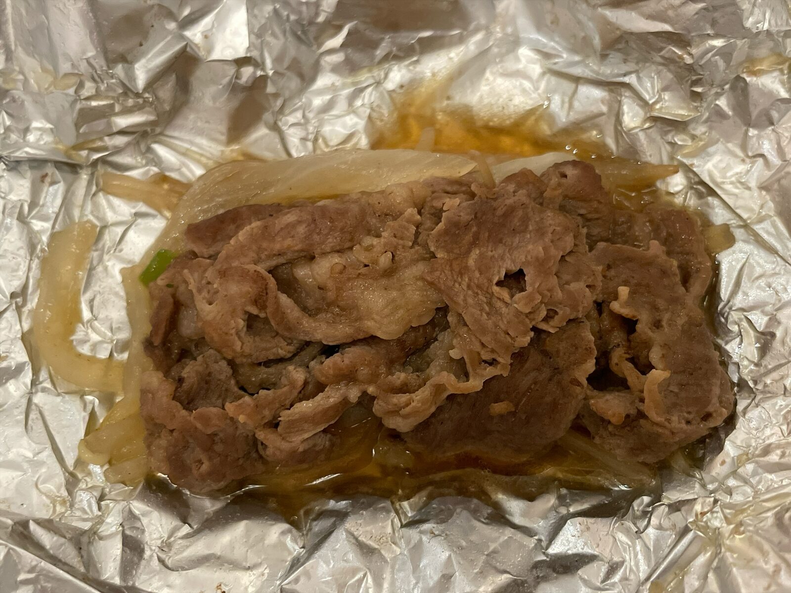 開いたアルミホイルの中の、薄切りの肉と玉ねぎの蒸し焼き