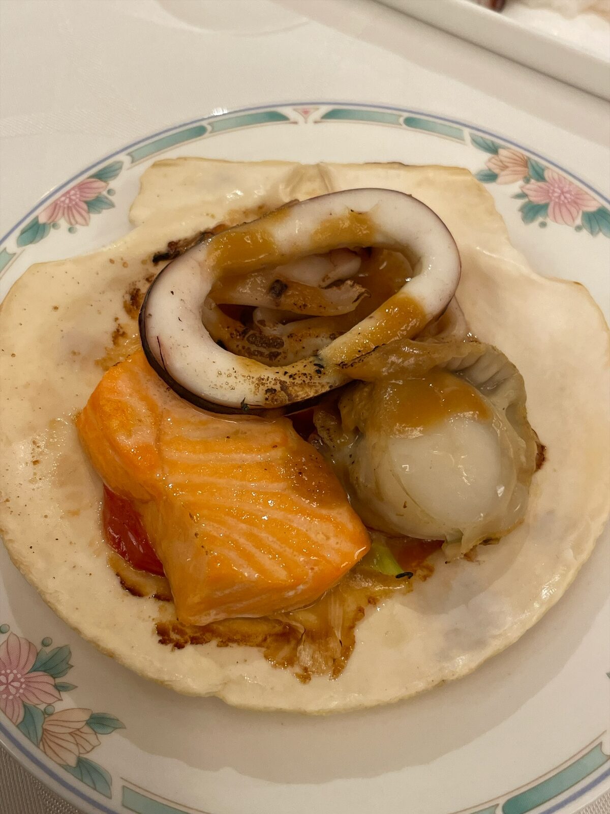 ホタテの貝殻に、焼いたサーモン、ホタテの貝柱、イカを盛り、茶色いタレをかけた一皿