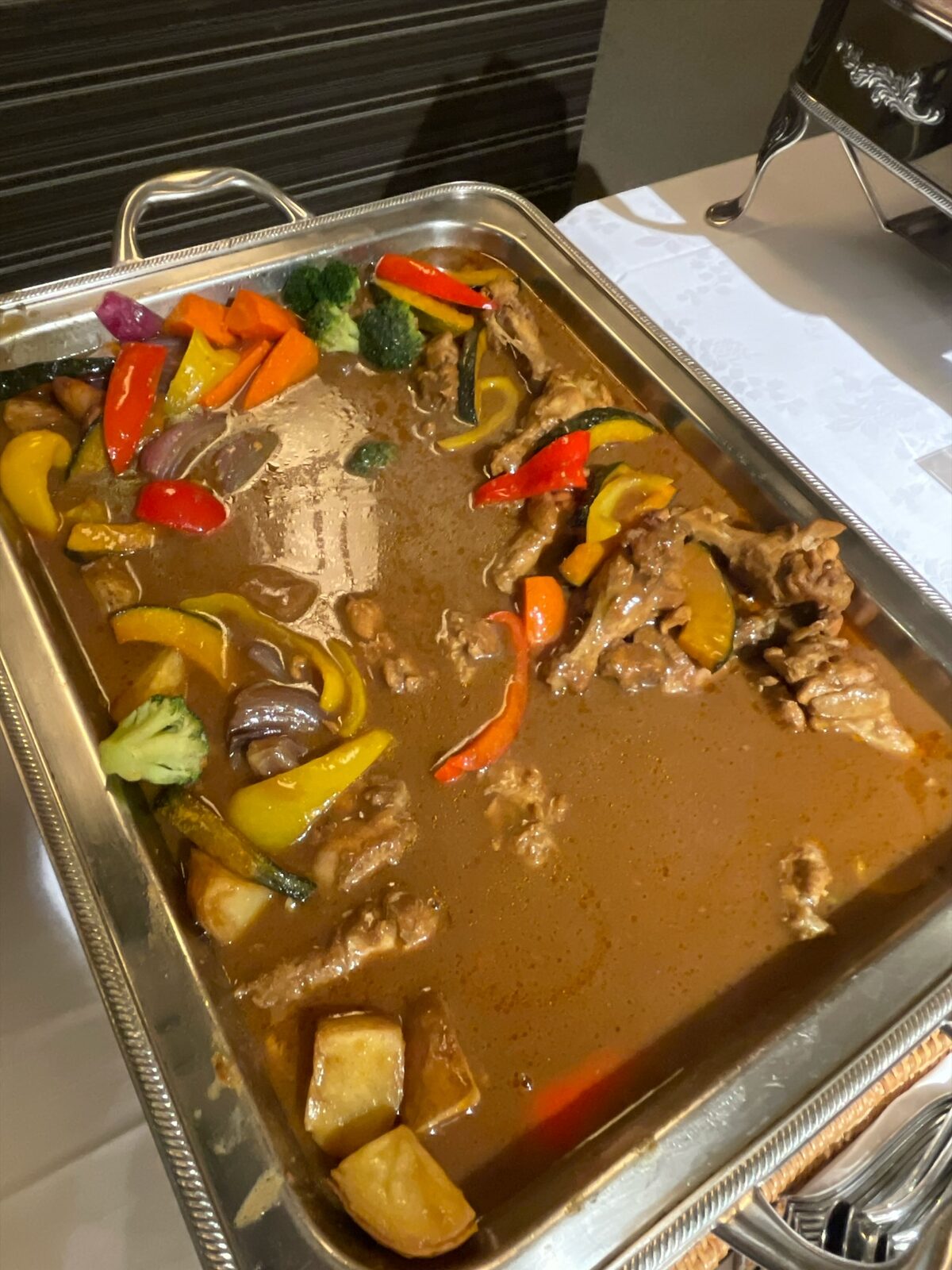 銀色の角バットのスープカレー。鶏肉、かぼちゃ、赤と黄のパプリカ、ブロッコリー、じゃがいもが入る