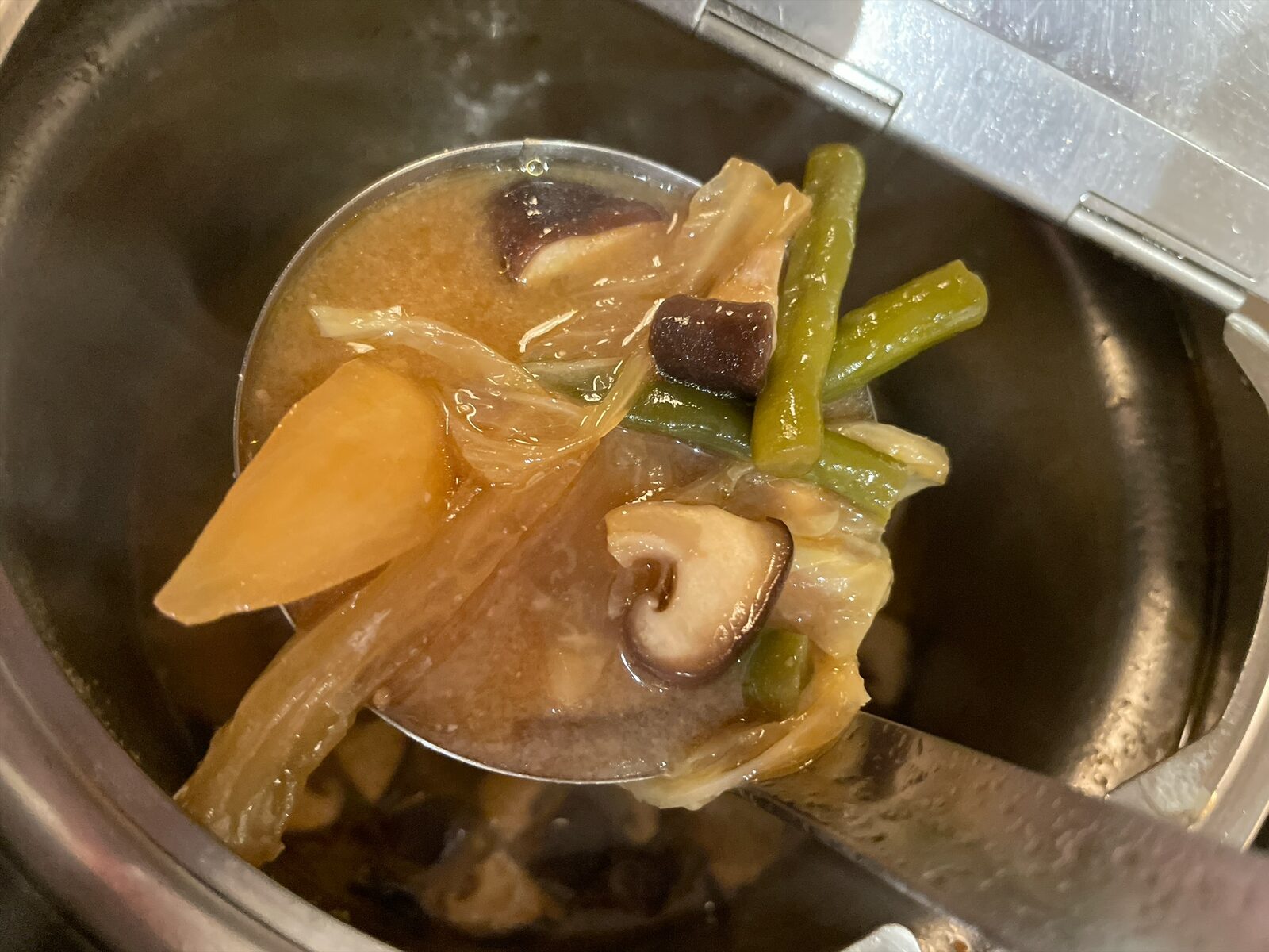 保温鍋からお玉ですくった味噌色の汁物。大根、白菜、しいたけ、いんげんが入っている