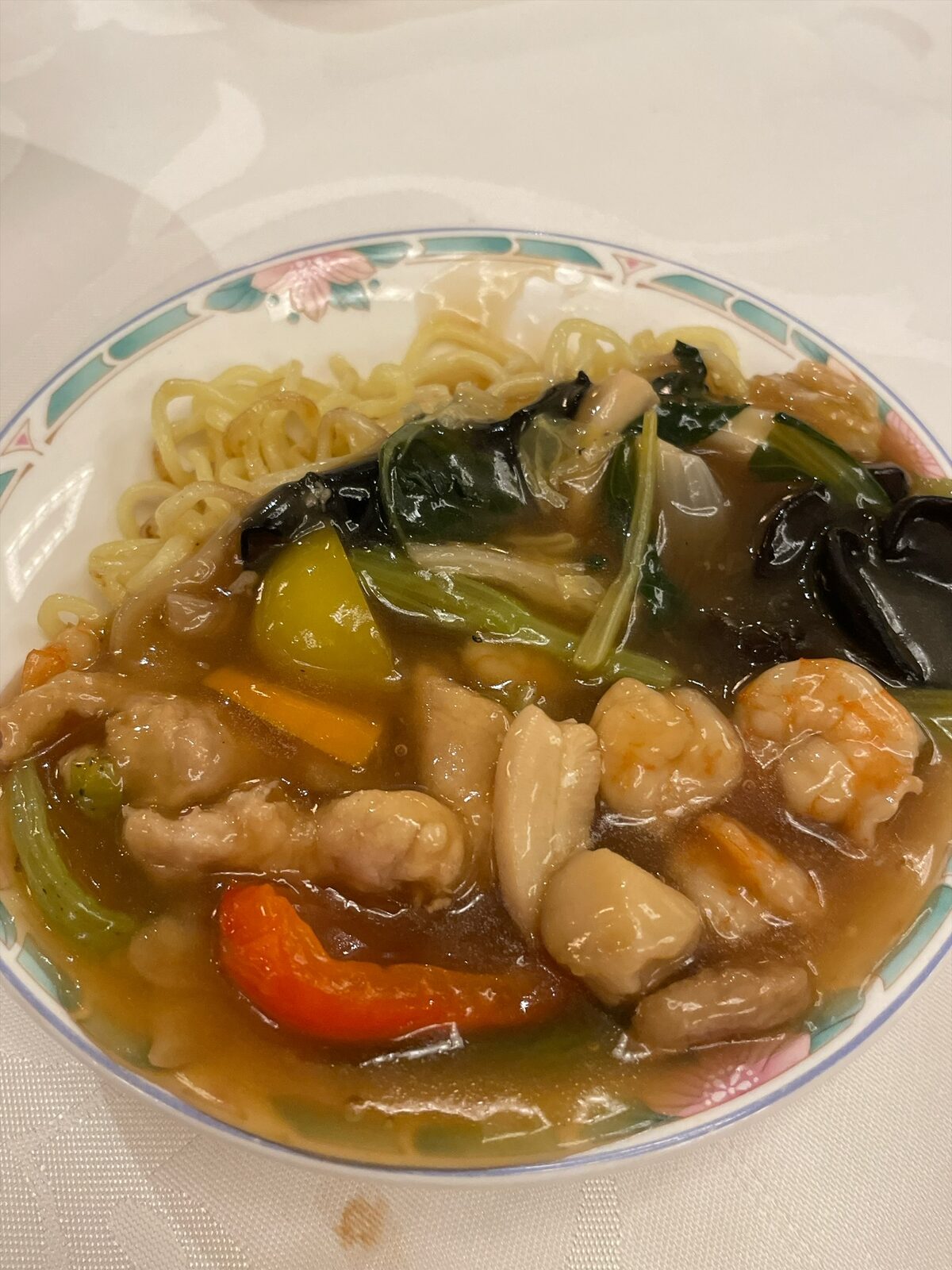 花柄の皿の中華麺に、エビ、ホタテ、イカ、きくらげ、青菜、パプリカ入りのあんをかけた一皿