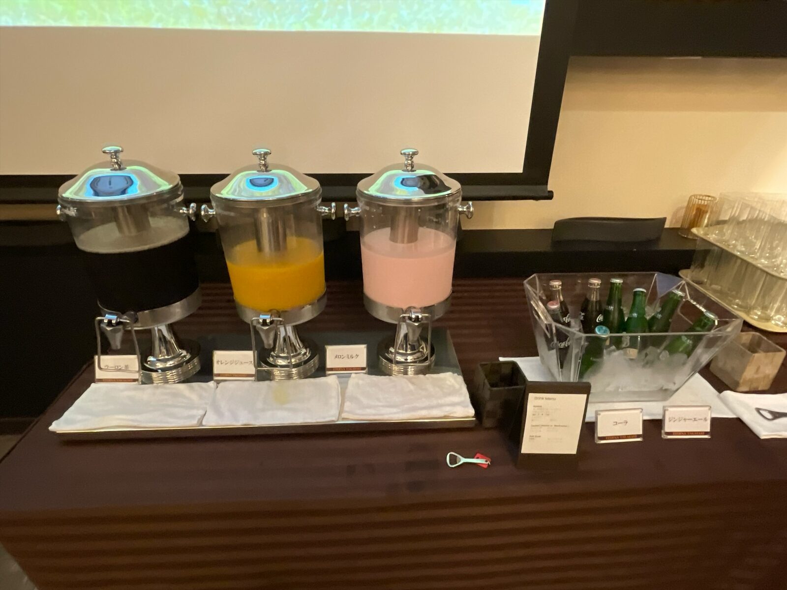 3台のドリンクディスペンサー。左から烏龍茶、オレンジジュース、ピンク色のメロンミルク。右に氷で冷やした瓶
