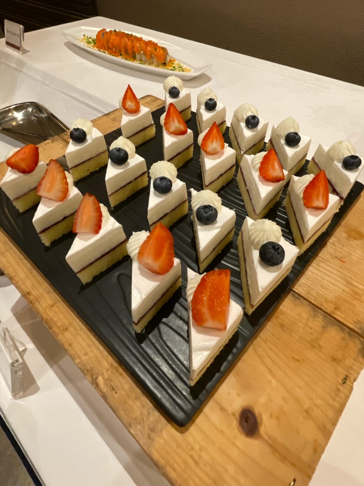 黒い板皿に並んだ三角形のレアチーズケーキ。いちごまたはブルーベリーと絞りクリームがのる