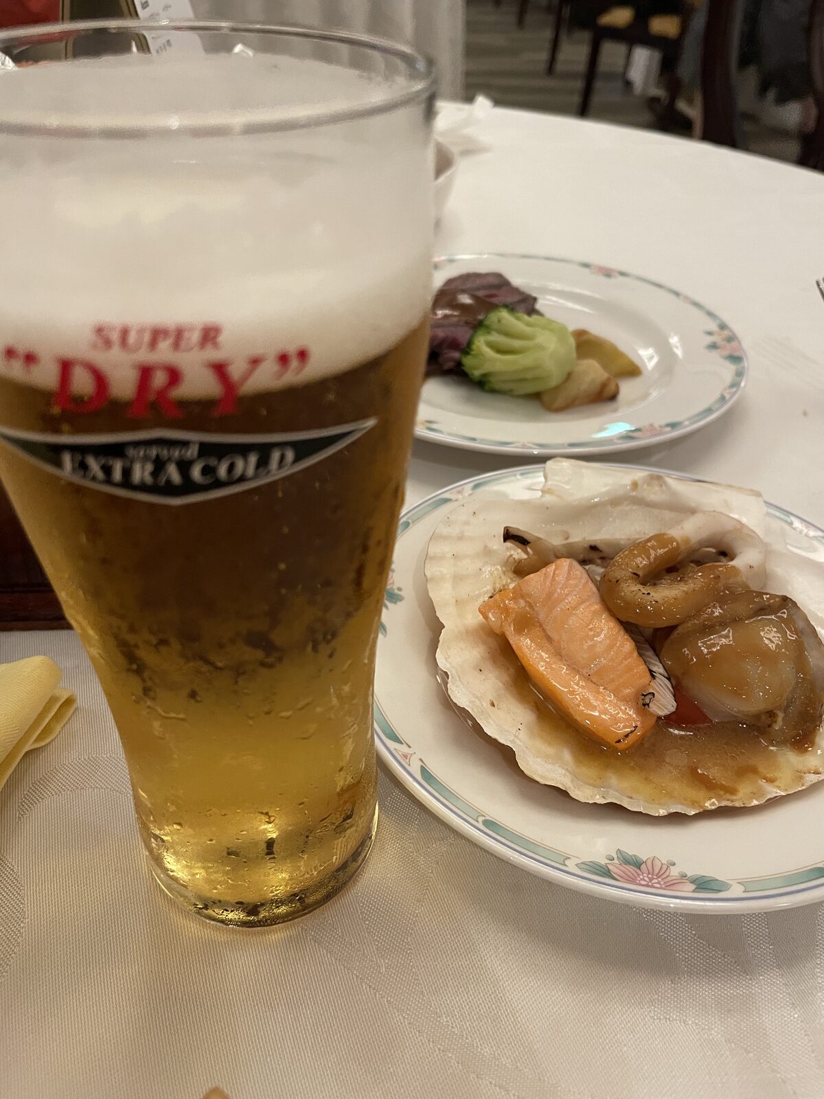 泡の立った生ビールのグラスと、ホタテの貝殻に盛った魚介の焼き物