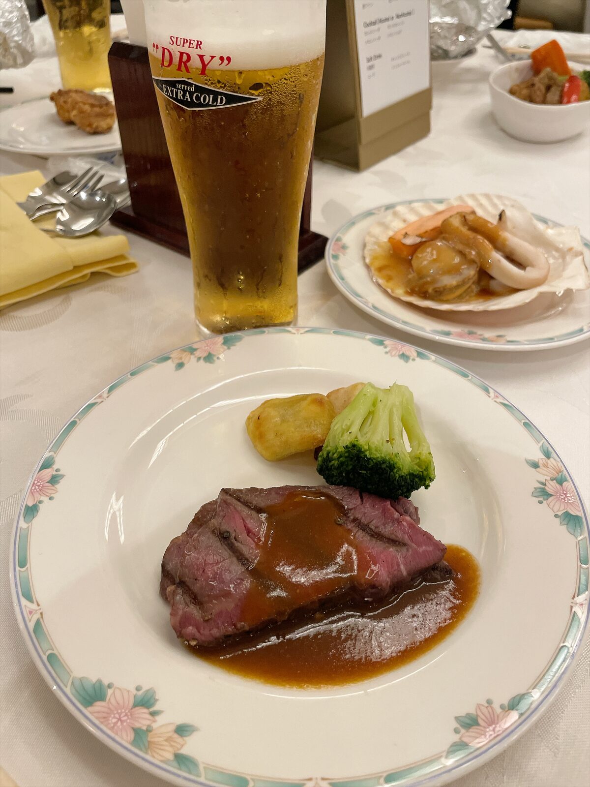 花柄の皿に盛った赤身のステーキに茶色いソース。付け合わせにブロッコリーと焼いたじゃがいも