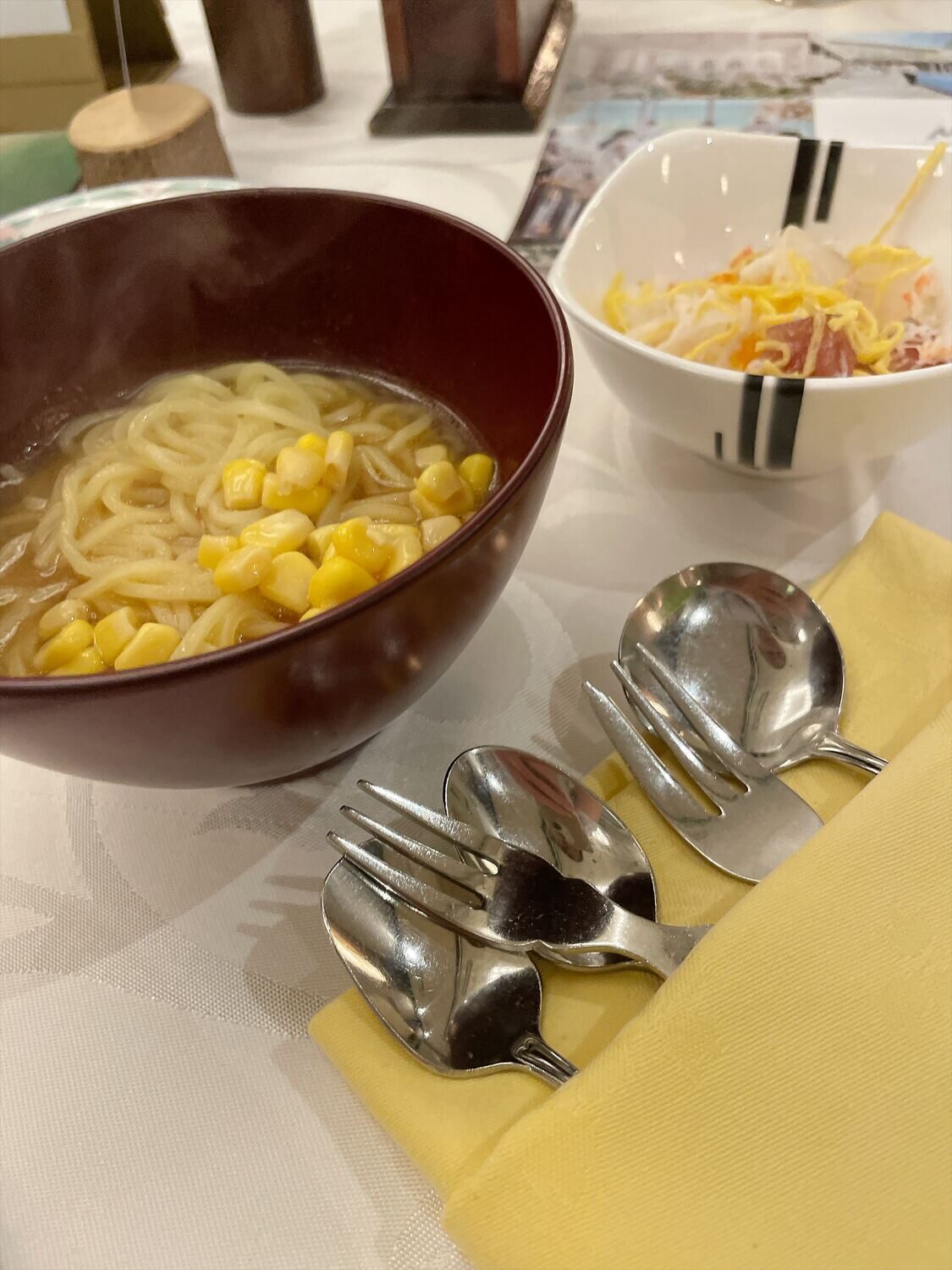 赤いお椀のコーン入りラーメンと、小鉢のちらし寿司。手前に小さめのフォークとスプーンが2組